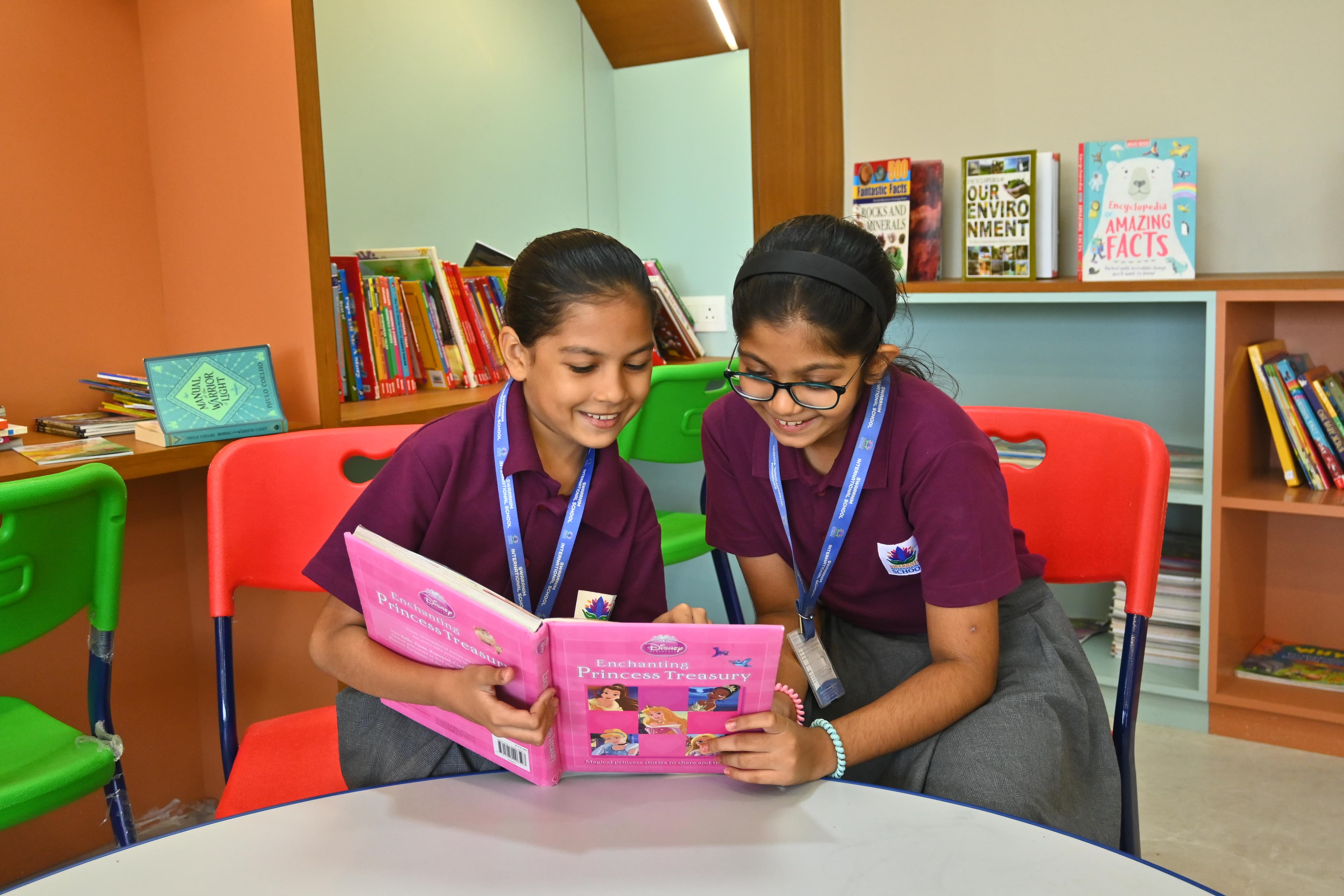 Two girls sharing a book while sitting on cosy bean bag chairs by the window